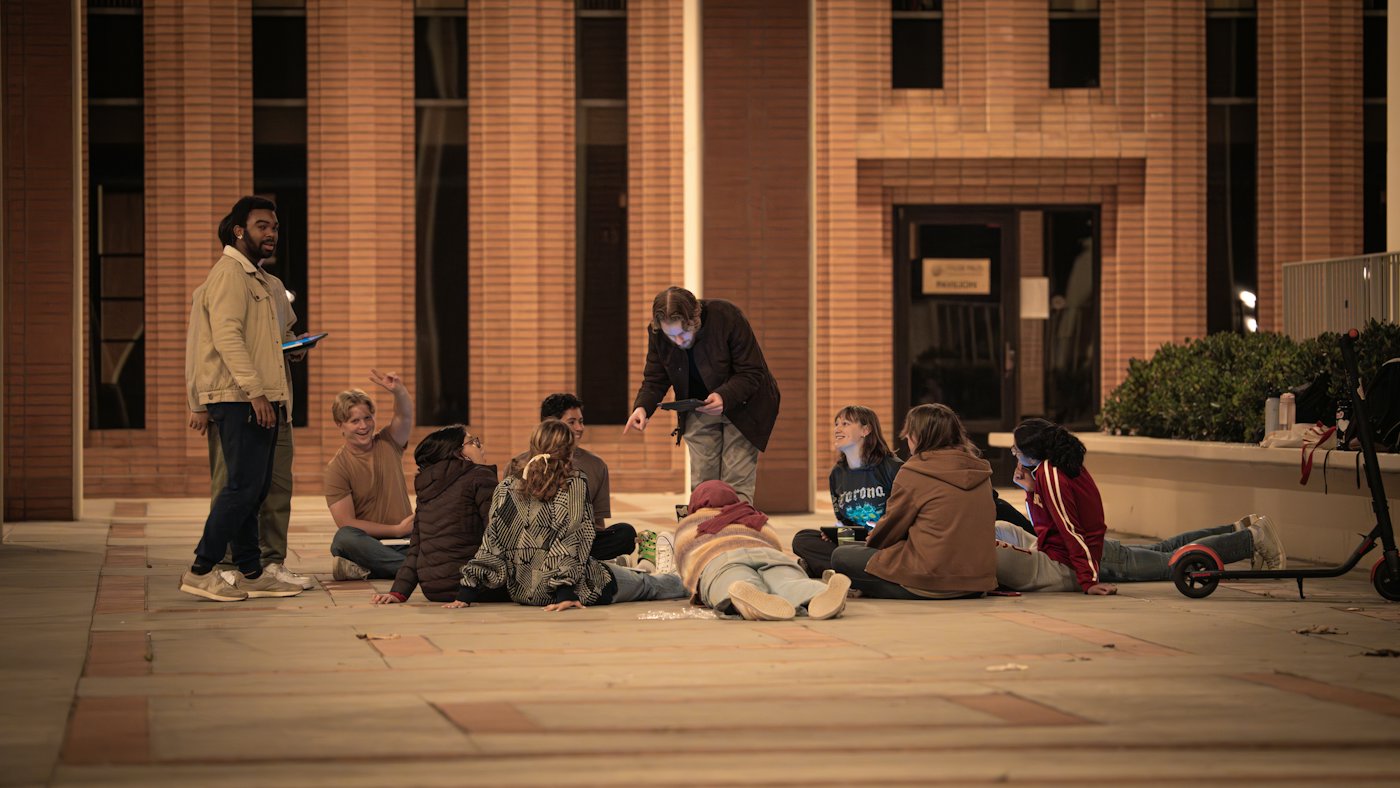 A community group sitting together outside in the evening, talking and sharing a tablet