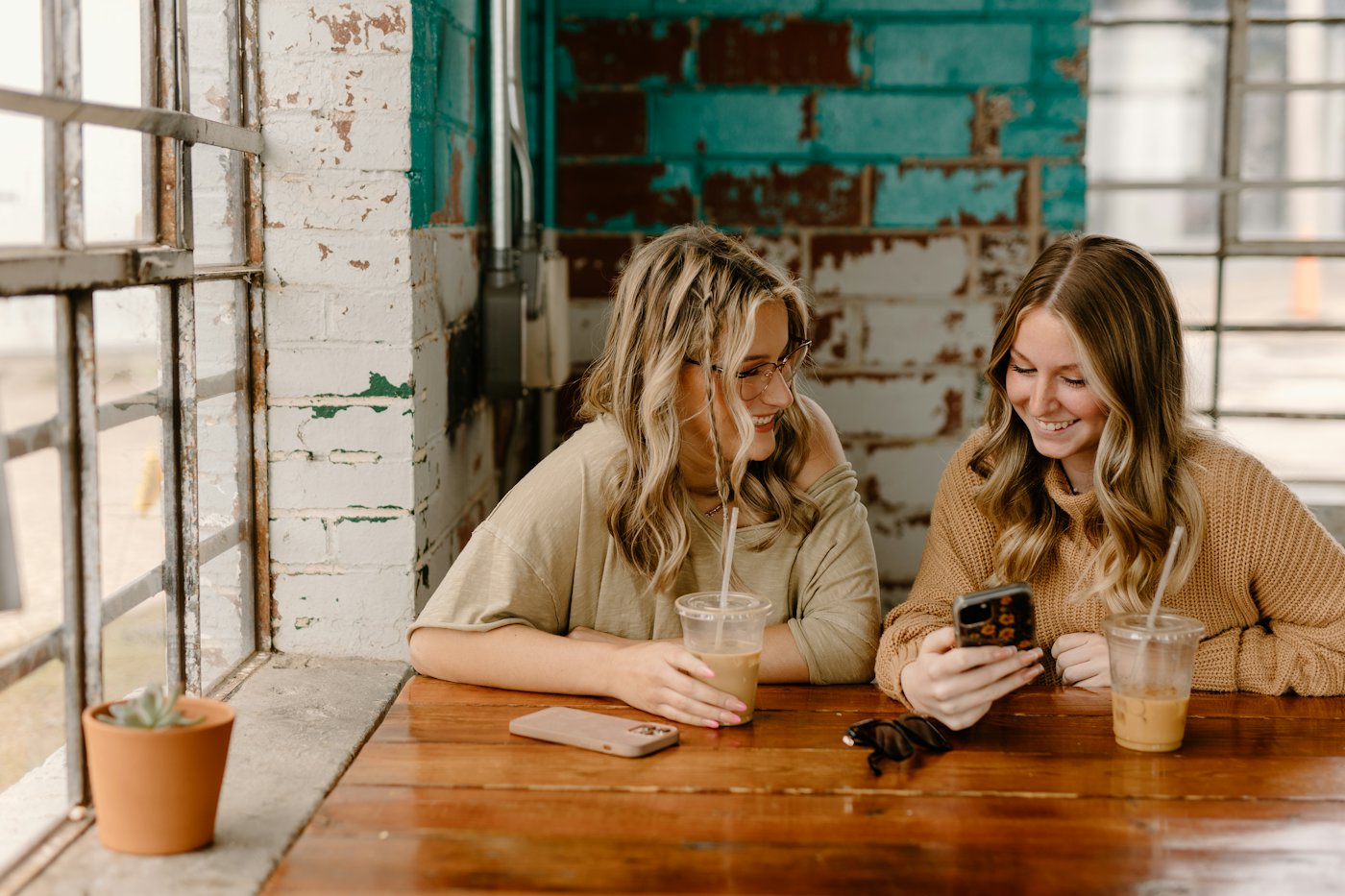 Two friends at a cafe table laughing at something on a phone