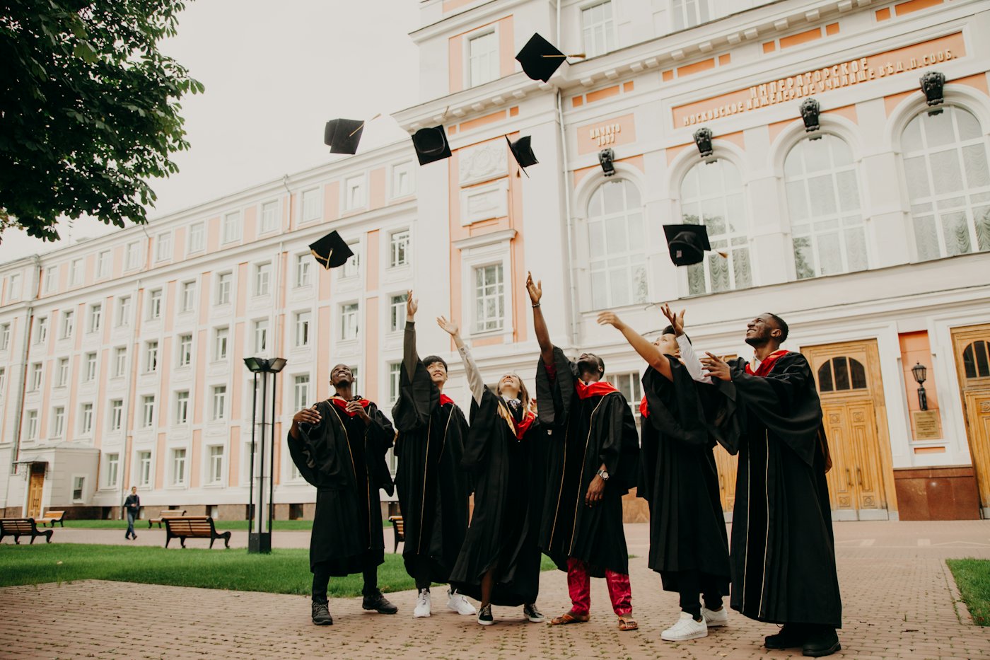 A group of graduates in black gowns throwing their caps in the air outside a university building