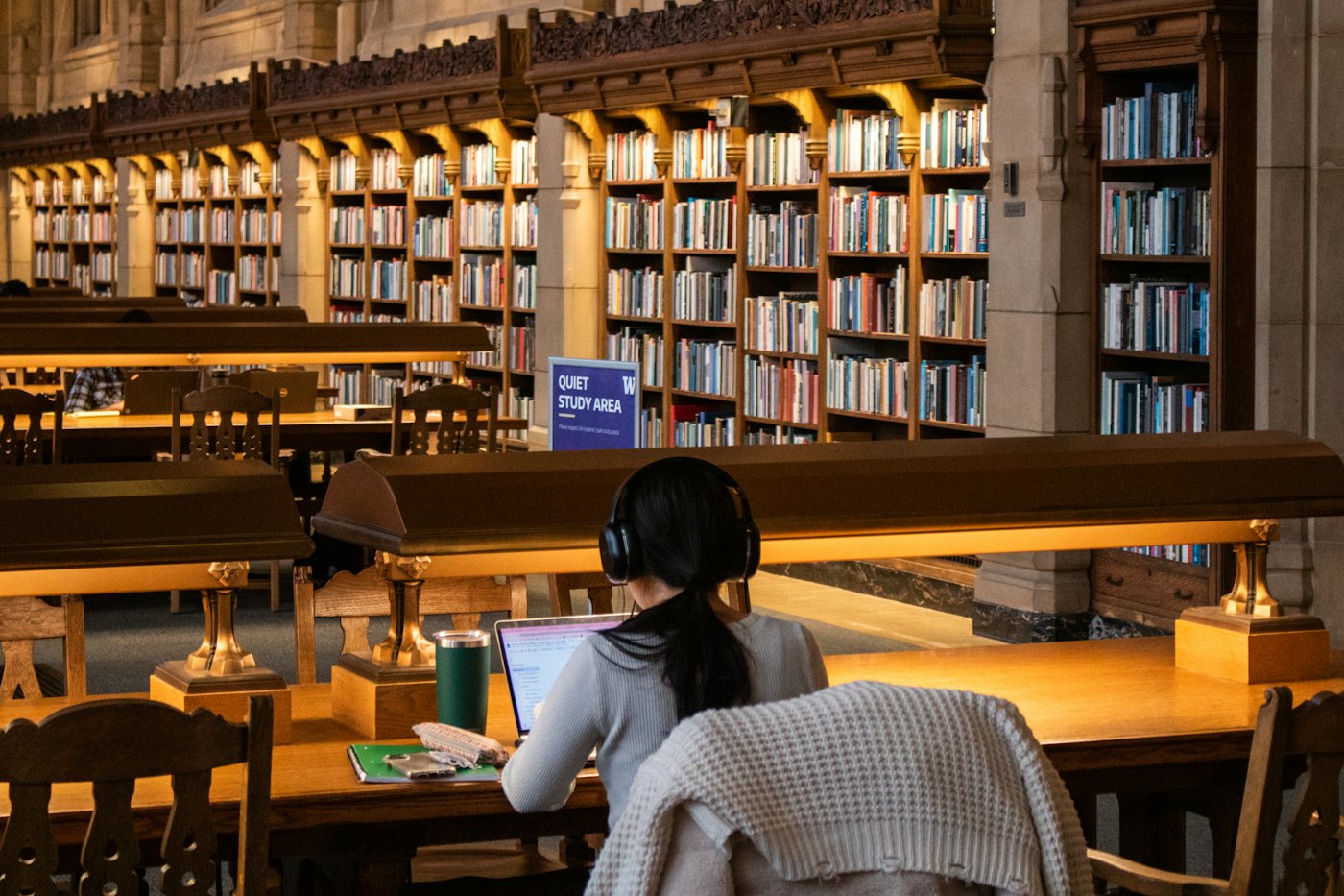 A student with headphones studying in a large wood-panelled library
