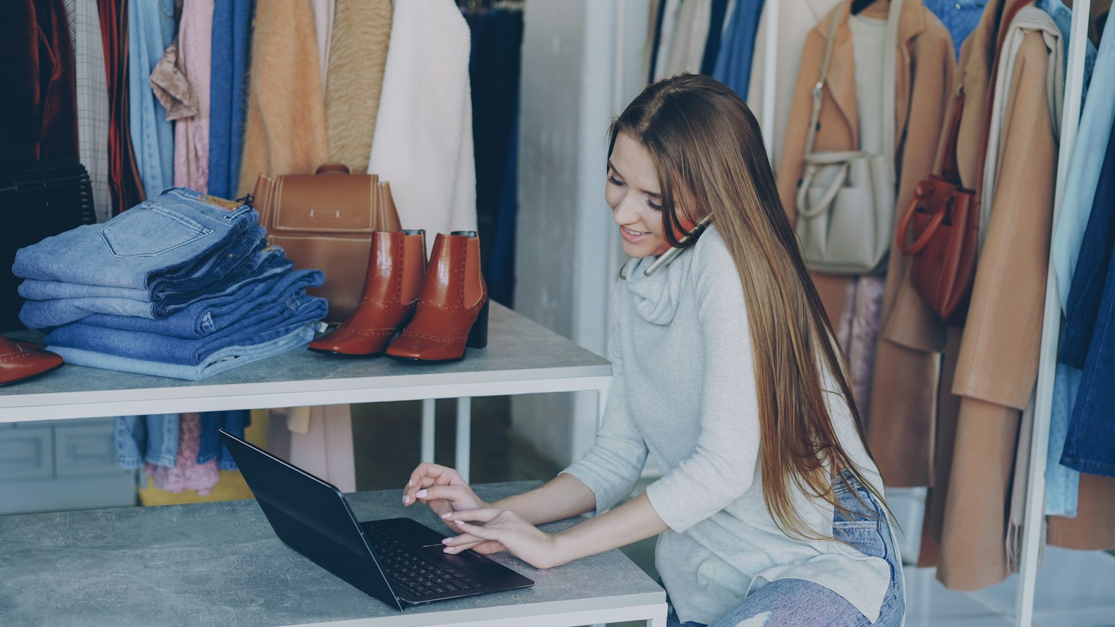 A shop owner on the phone at her laptop in her clothing store