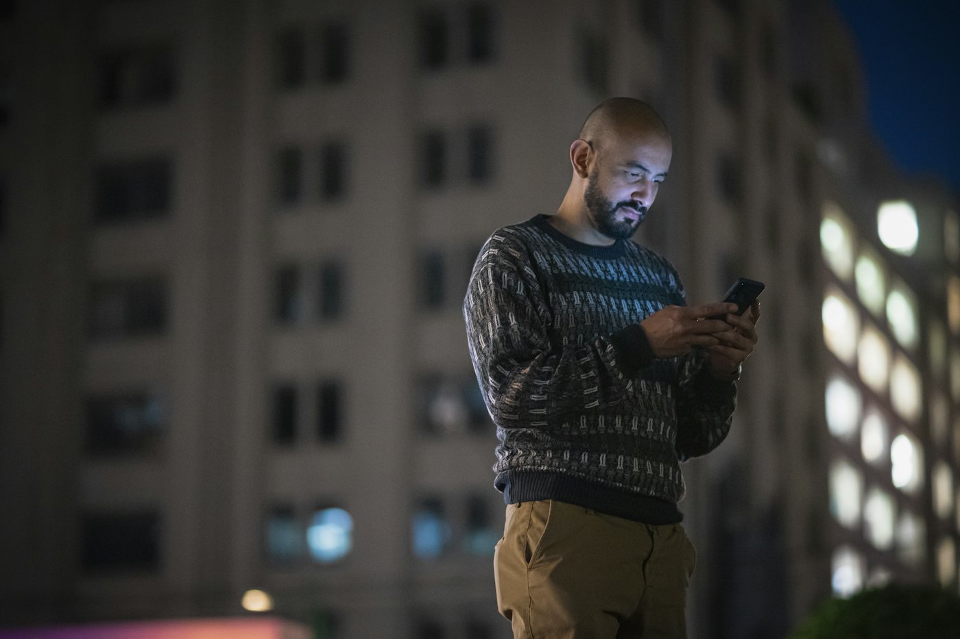 A man checking his phone outside a building at night
