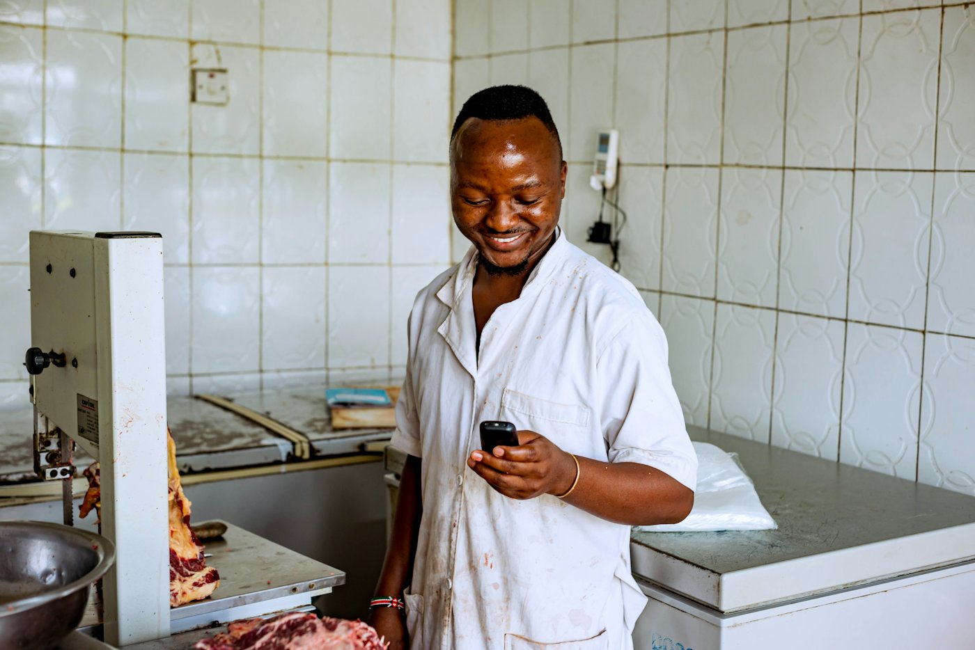 A food business owner in his kitchen, smiling at his phone